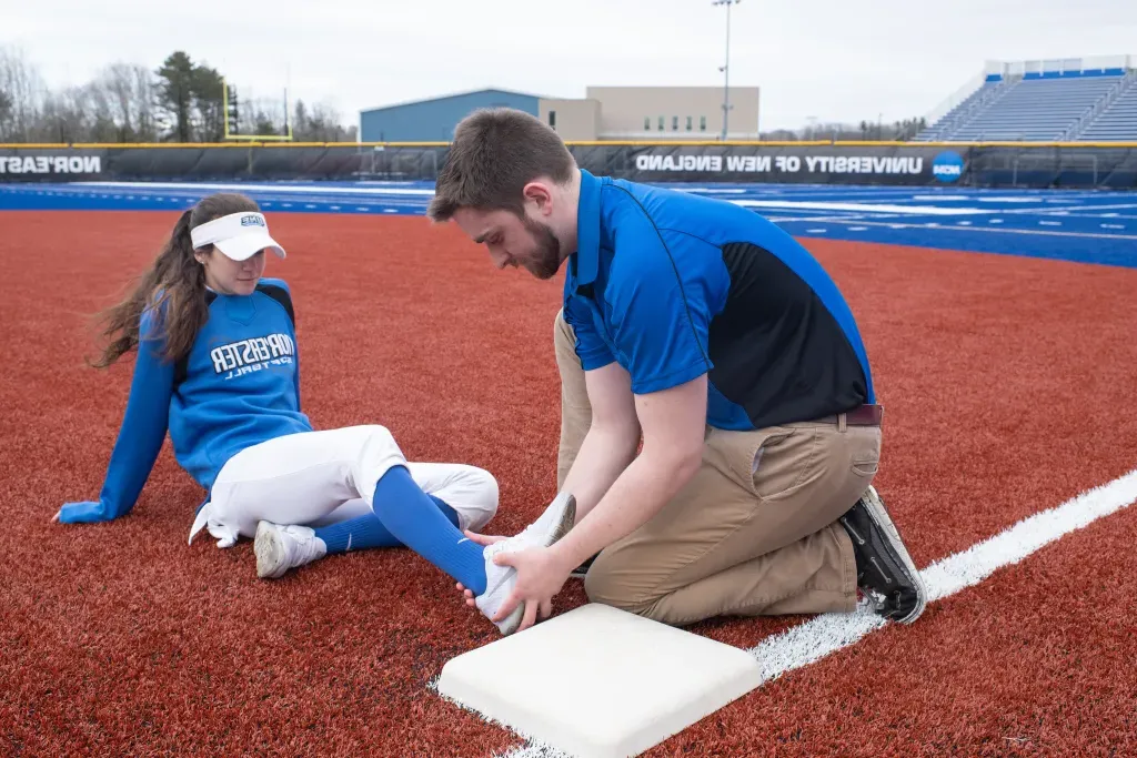 An athletic training student assists a baseball player out on the field