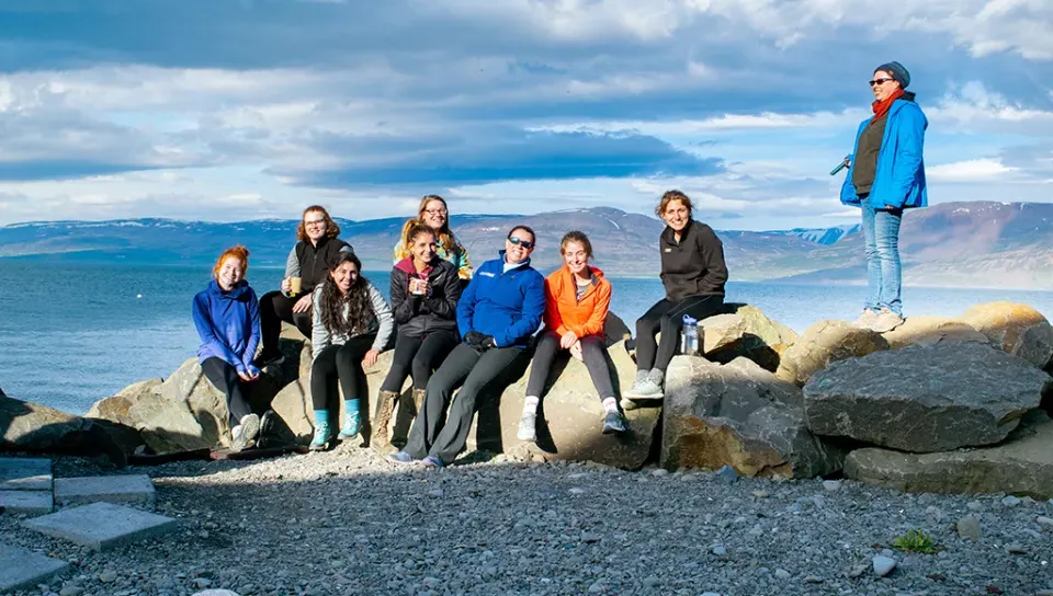 A group of students sit near the ocean in Iceland