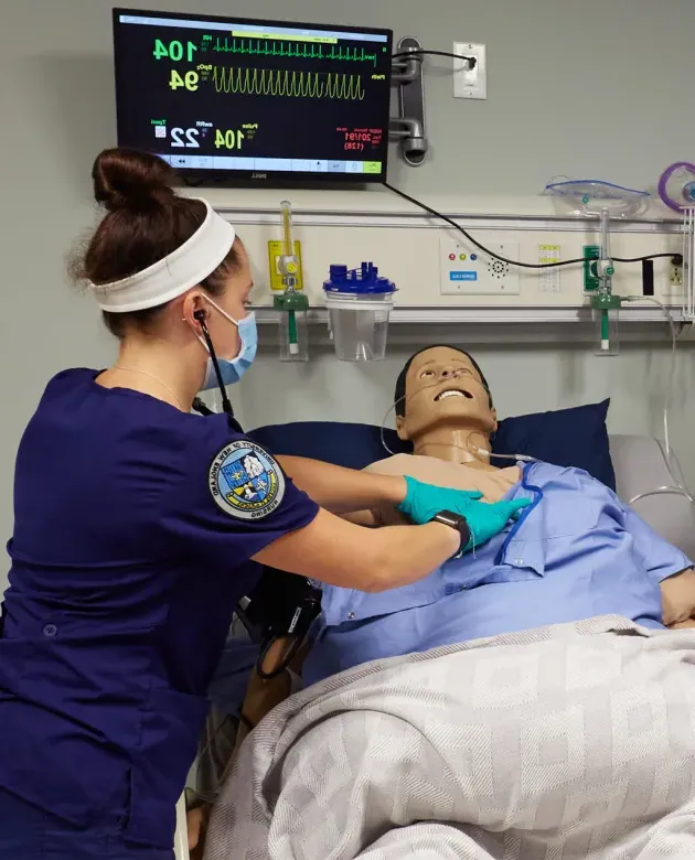 A nursing student assists a patient simulator in the simulation lab