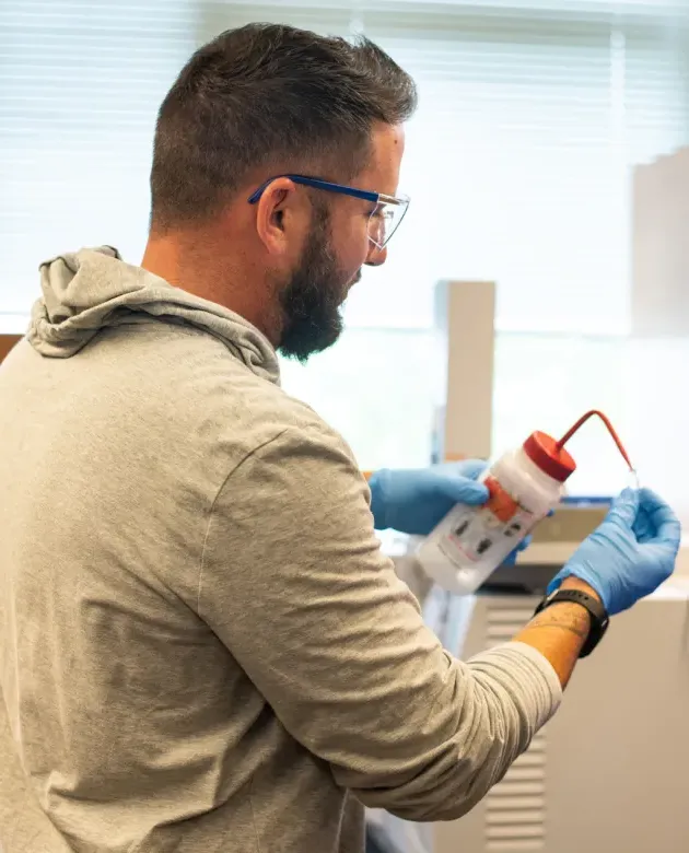 A chemistry student squeezes liquid into a small test tube from a bottle