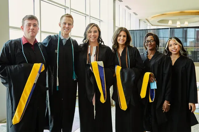 Six graduate students pose in their commencement robes